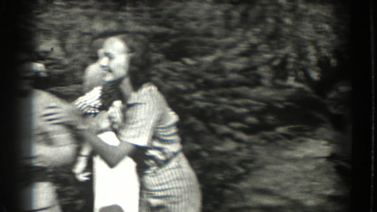 Two women playfully hold and spin another woman outdoors in soft black-and-white footage.