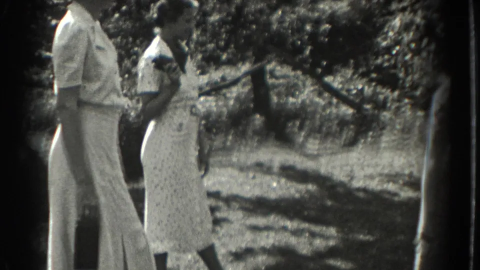 1937 Southampton frame showing two women standing outdoors, one in wide-leg trousers and one in a patterned dress, near shrubs and a fence or posts.