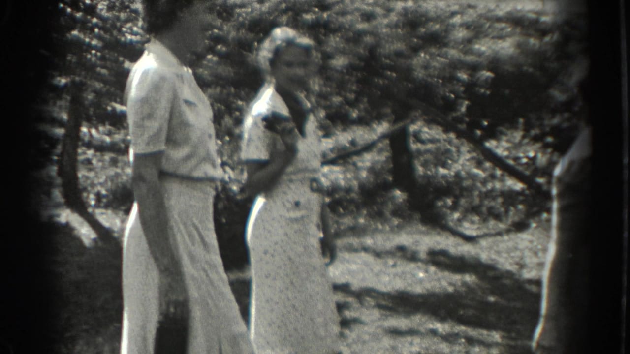 Two adult women stand outdoors in a shaded garden area.