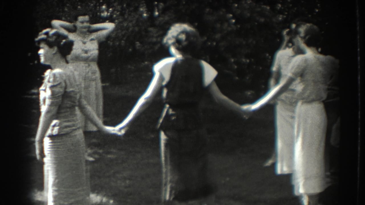 Women in dresses hold hands in a shaded backyard garden.