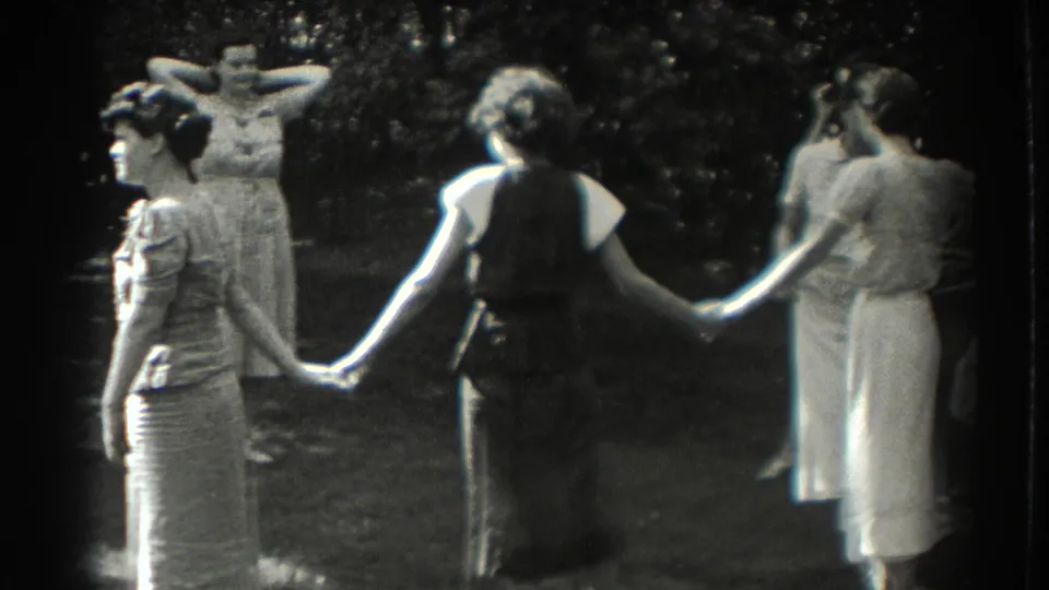 In 1937 Southampton home-movie footage, women in dresses hold hands in a backyard circle under trees.