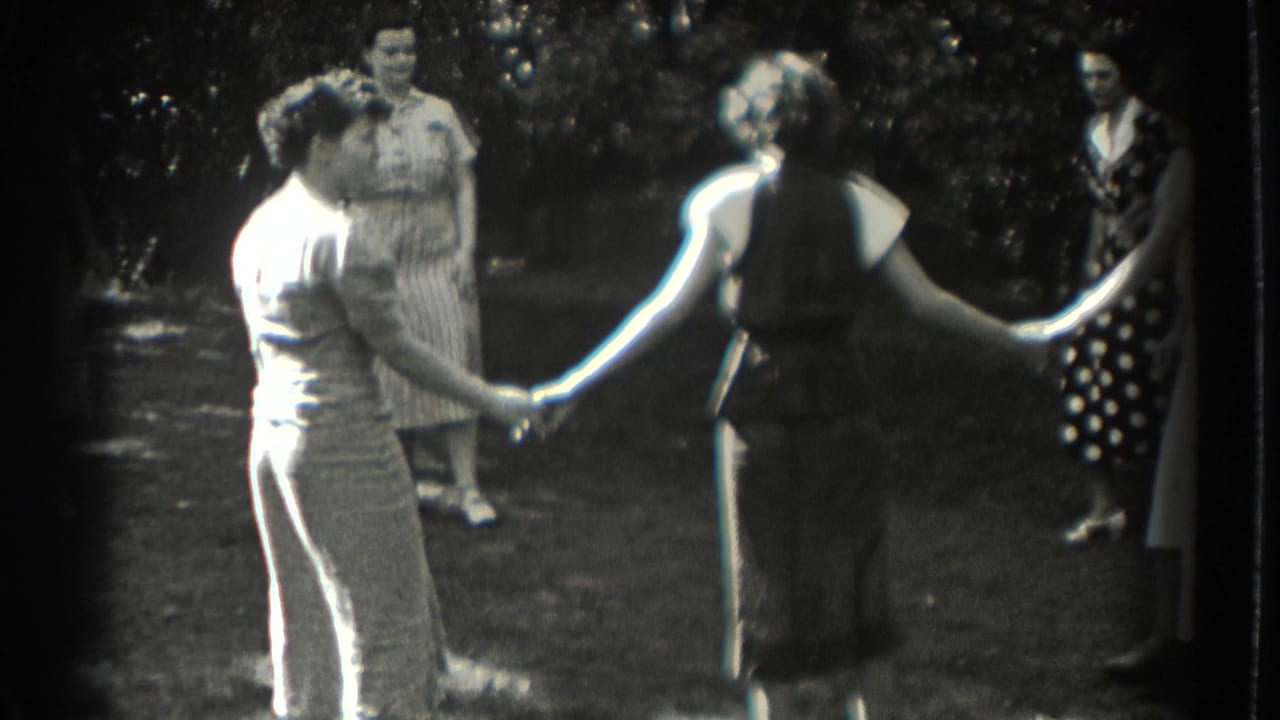 Two women clasp hands while others stand around a garden circle.