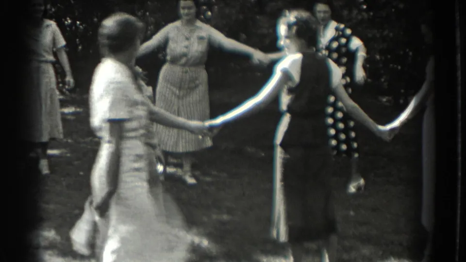 A woman in a light dress moves within a backyard circle of women holding hands in 1937 footage.
