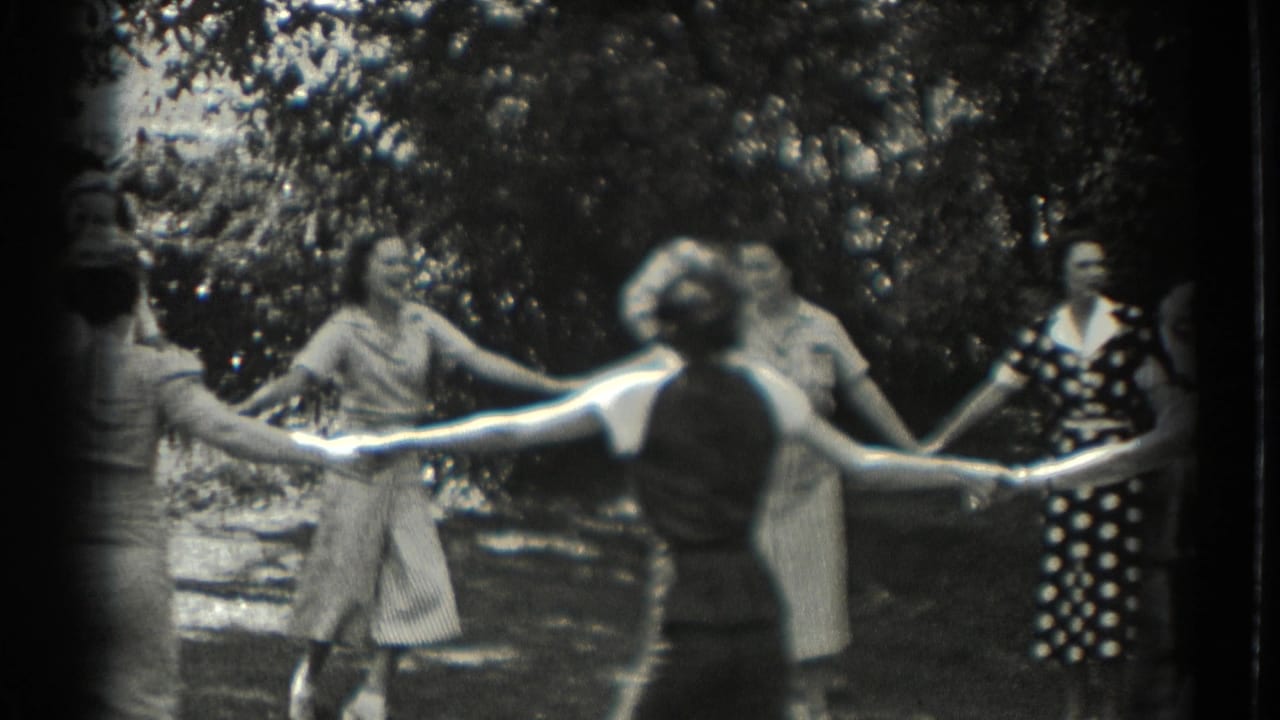 Women and girls hold hands in a garden circle game.