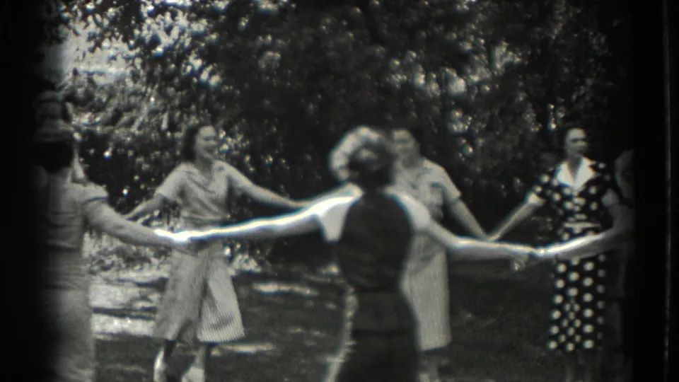 1937 Southampton home-movie frame showing women and girls holding hands while playing a ring game in a sunlit garden.
