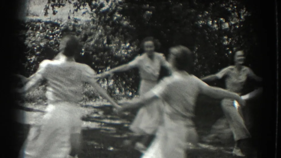 Women and girls in light summer clothing turn in a hand-held circle in 1937 Southampton garden footage.
