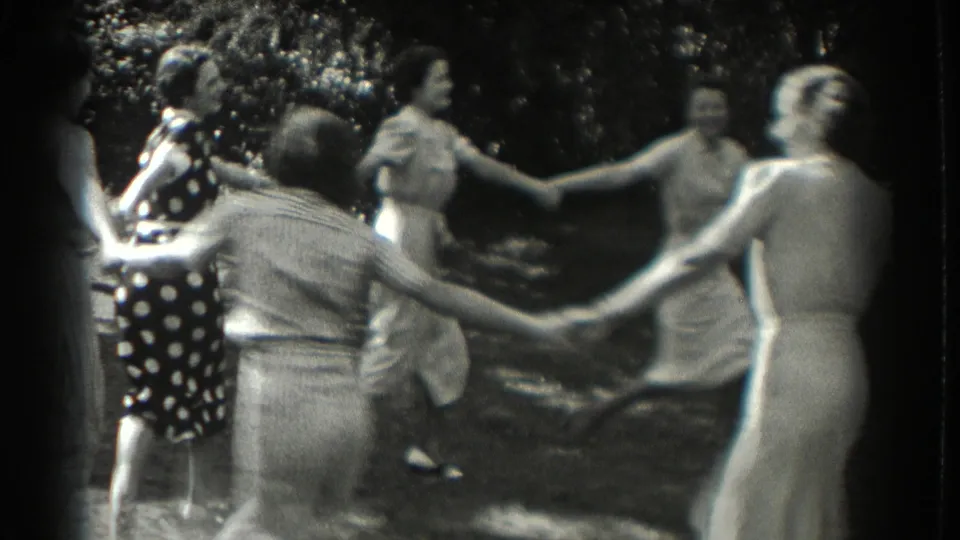 1937 Southampton frame of women and girls circling hand in hand, with foliage and dappled light behind them.
