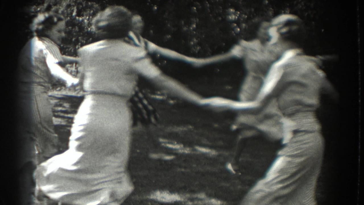 Women and teenage girls hold hands while spinning in a leafy backyard.