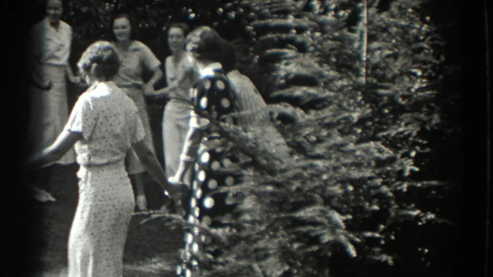 Women and teenage girls in 1930s dresses hold hands in a Southampton backyard at the end of the circular game.