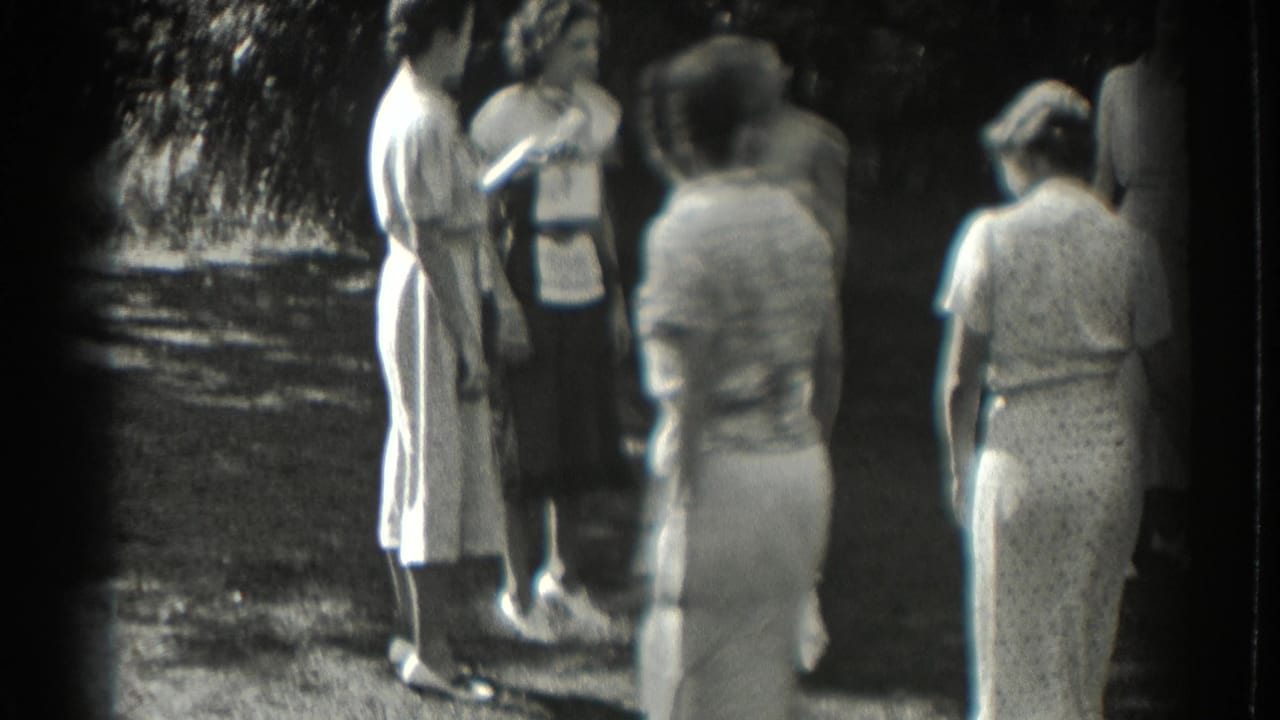 Women in light dresses stand together outdoors beside a shaded path.