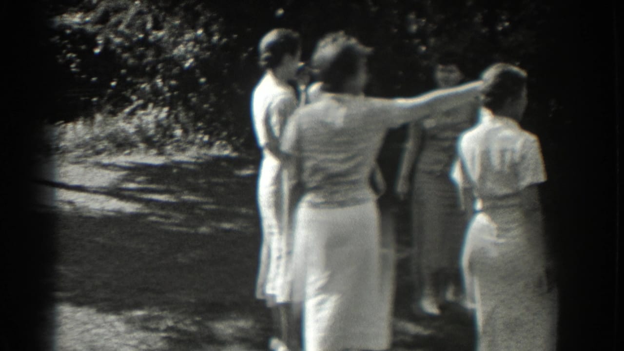 A woman gestures outward while others watch in a shaded outdoor area.