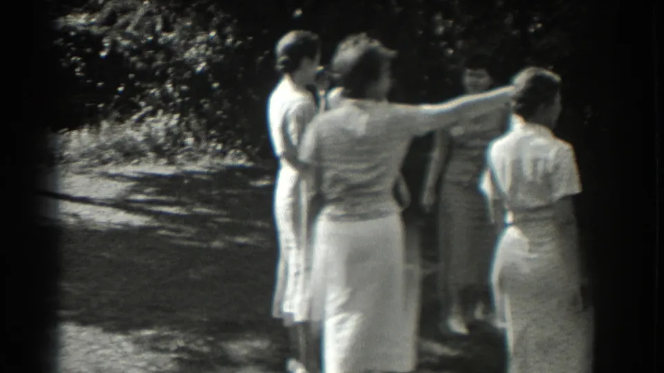 In 1937 Southampton home-movie footage, one woman points or gestures while several women stand nearby in a sun-dappled garden setting.