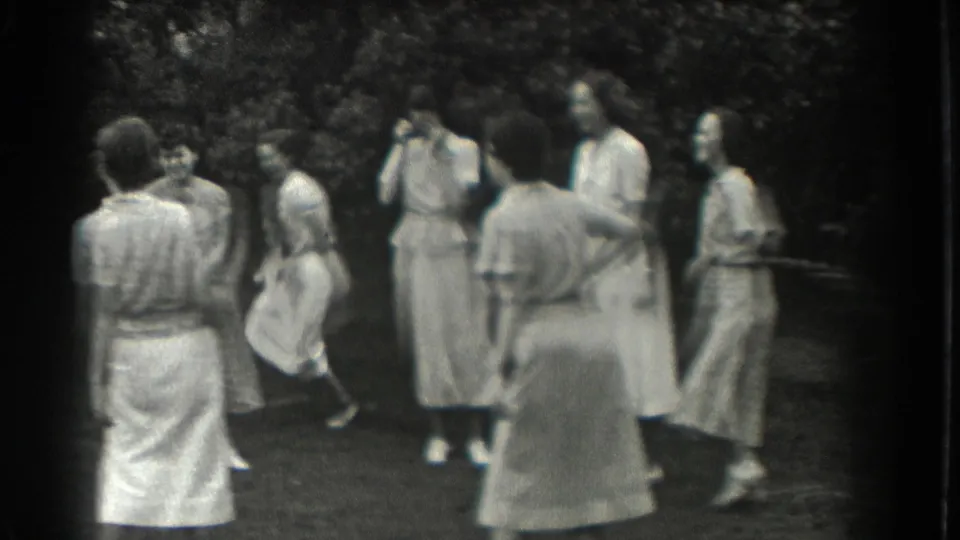 Women in period dresses gather in a shaded Southampton park as one woman runs or plays tag, matching the supplied church-sisters reunion context.