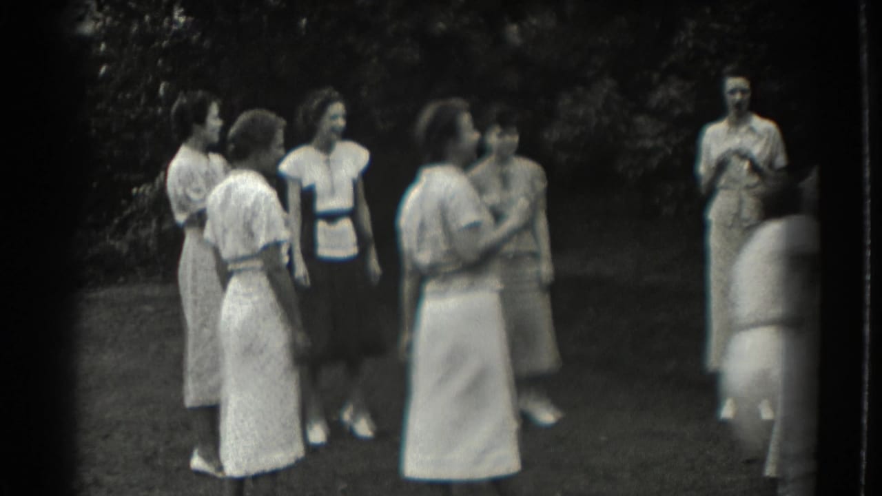 Several adult women stand together on a lawn during a game.