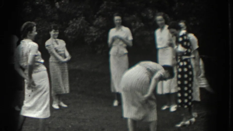 A woman bends forward during the lawn game while other adult women in dresses look on in Southampton.