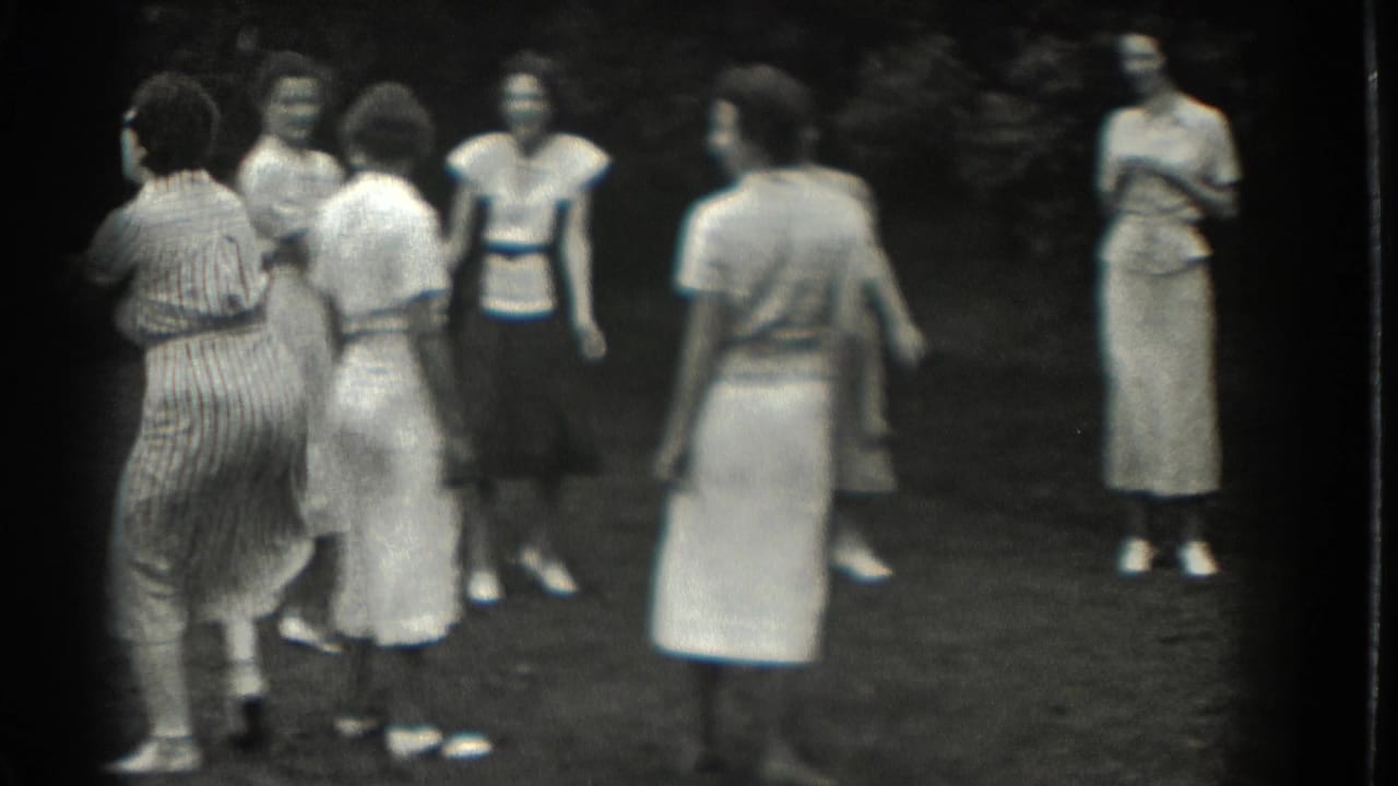 Women in dresses and skirts stand on a grassy lawn during an outdoor gathering.