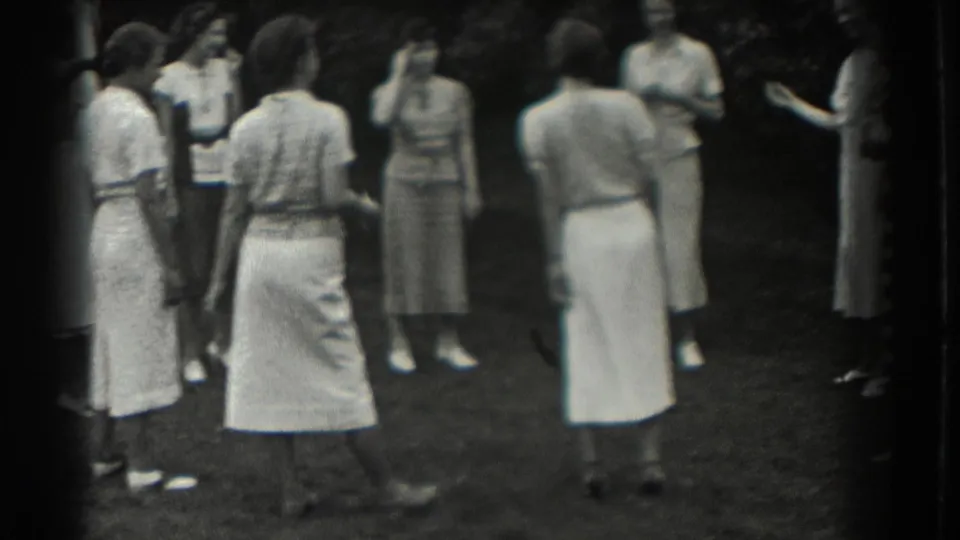 Women in skirts and dresses stand in a loose circle on a Southampton lawn, captured in soft 8mm focus.