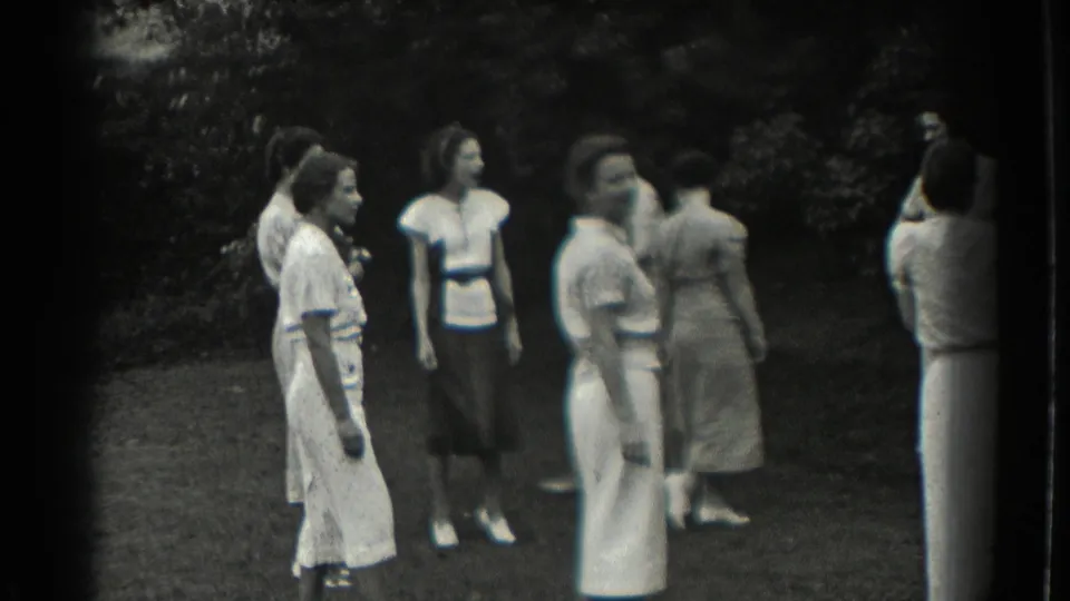 Several women in period dresses move and watch one another during an informal outdoor game in Southampton, 1937.