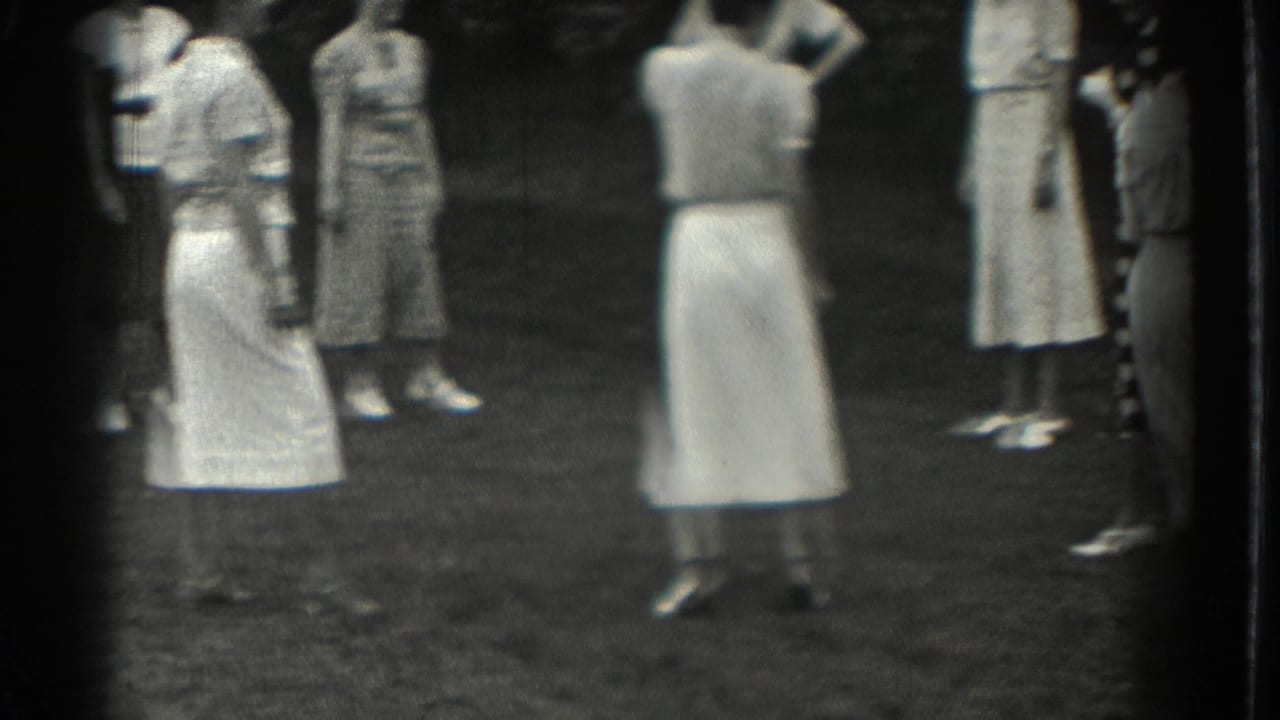 Women in light dresses stand spaced apart on a grassy lawn.