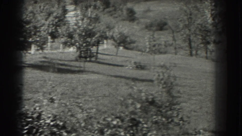 Black-and-white 1937 home-movie frame showing a quiet Southhampton landscape with open lawn, trees, and long shadows.