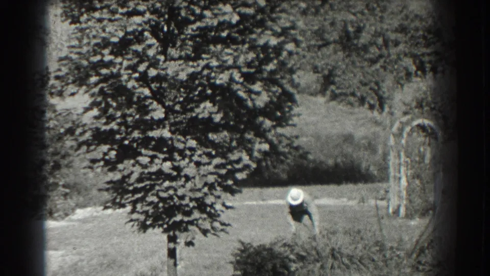 1937 Southampton frame showing a distant person in a wide-brimmed hat bending near a pale field edge or path.