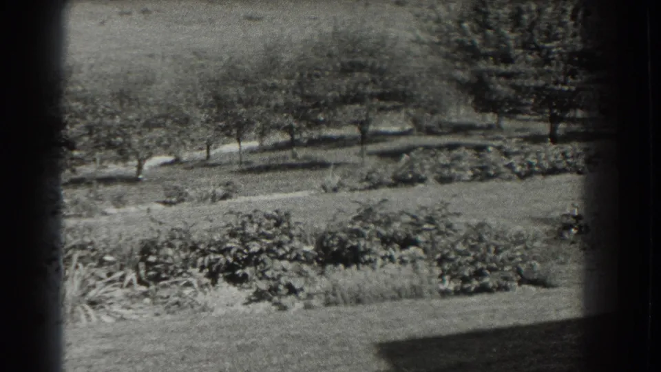 1937 Southampton home-movie frame showing a landscaped garden, lawn, shrubs, and trees through a dark 8mm border.