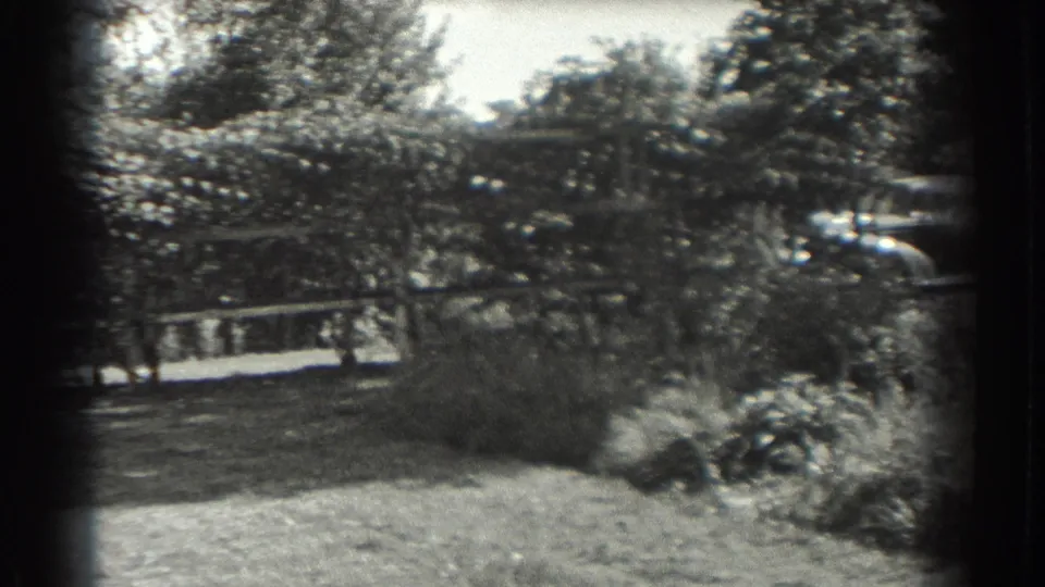 1937 Southampton residential garden view showing dense bushes, trees, low fencing, open yard, and a car partly visible at right.