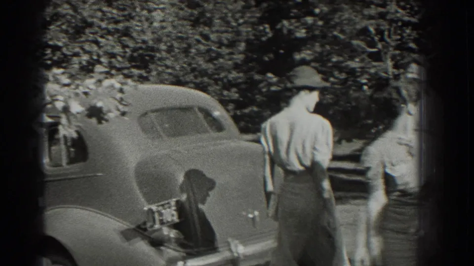 Two young women walk away from the camera near the rear of a parked classic car in Southampton, New York, in 1937.