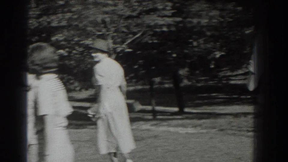 Two women in period dresses and hats walk through a leafy Southampton park in 1937 home-movie footage.