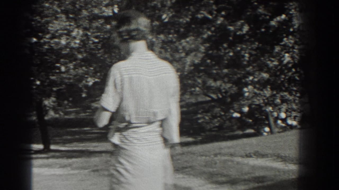 A woman in a light dress and hat walks away from the camera in a leafy Southampton park setting.