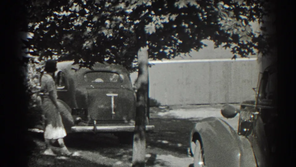A woman stands by the back of a rounded automobile in Southampton, with another car partly visible at the edge.
