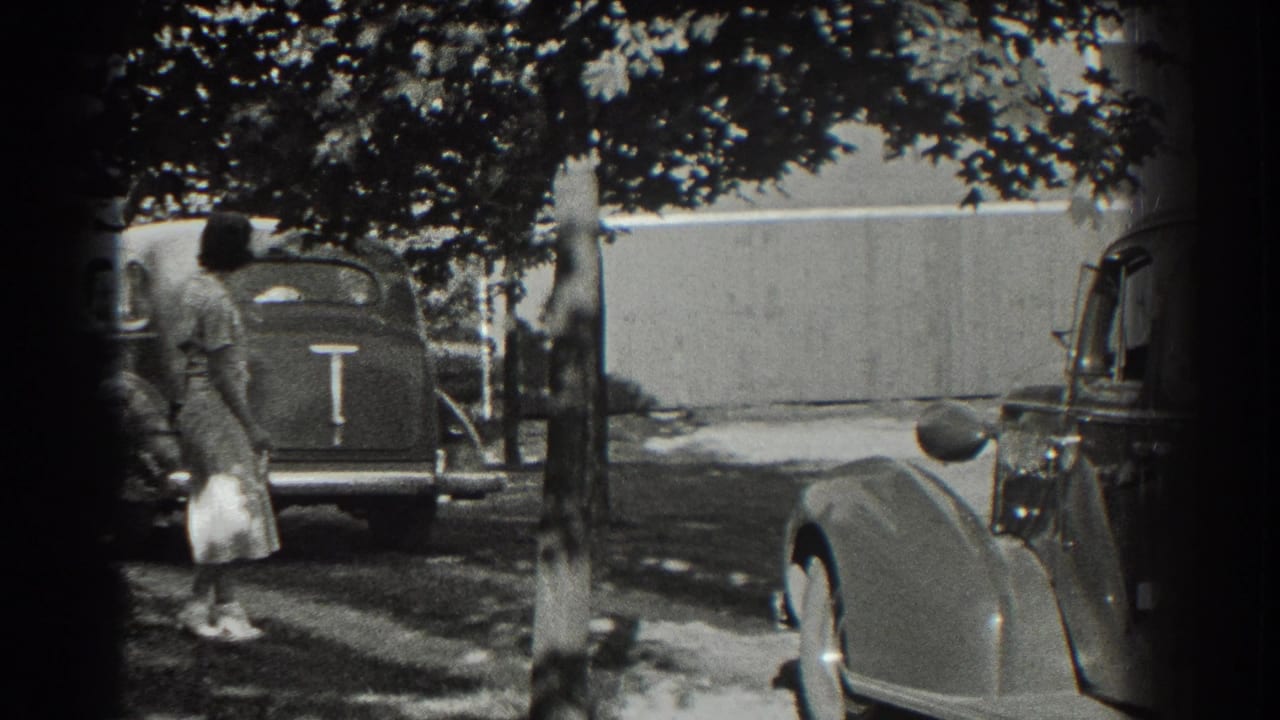 Woman walking near parked 1930s cars on a shaded driveway.