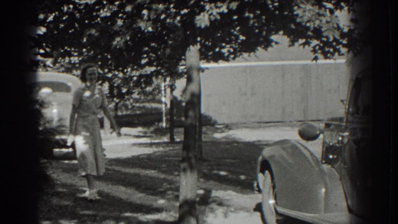 Woman walking toward the camera between trees and parked cars.