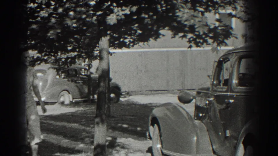 A rounded 1930s car begins moving through the Southampton driveway while the woman is partly visible near the lower left edge.
