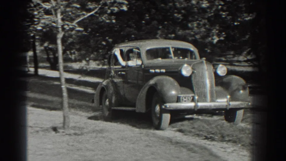 The 1930s sedan moves closer on the Southhampton driveway, with occupants faintly visible through the windshield and side windows.