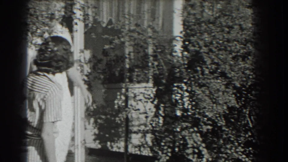 Two adult women in light dresses stand near leafy planting and a house or porch exterior in the supplied 1937 Southampton footage.