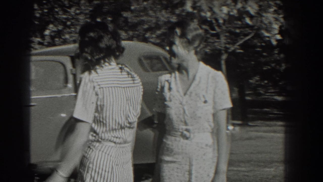 Two young women standing near a parked rounded car in dappled outdoor shade.