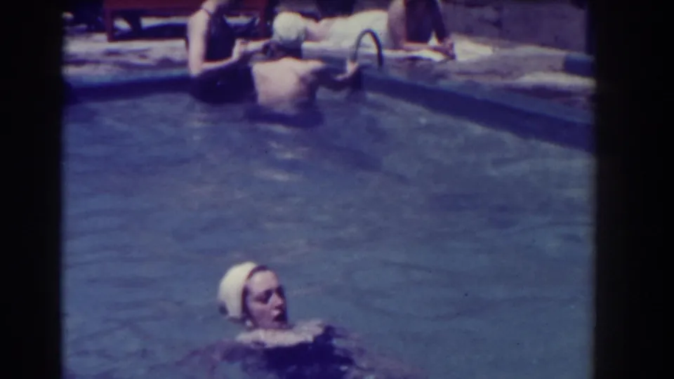 A woman wearing a white swim cap floats on her back in the pool while others remain near the edge.