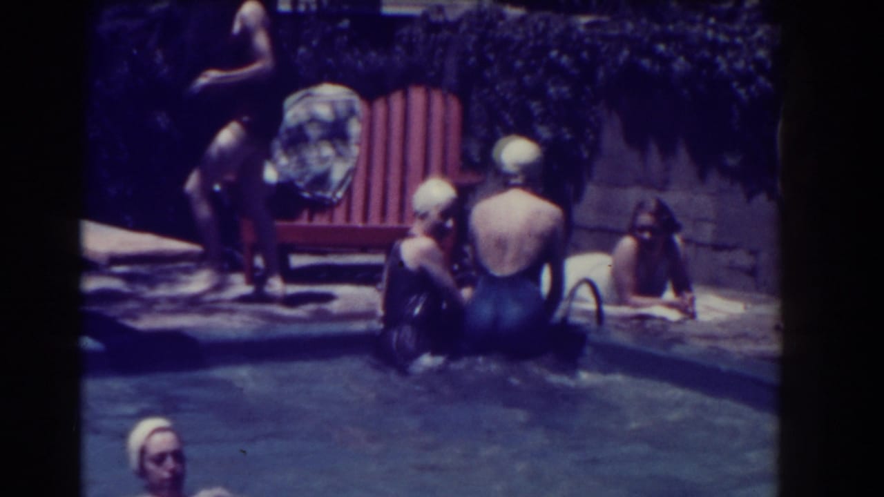 Several women in swim caps are near the pool edge and patio chair.