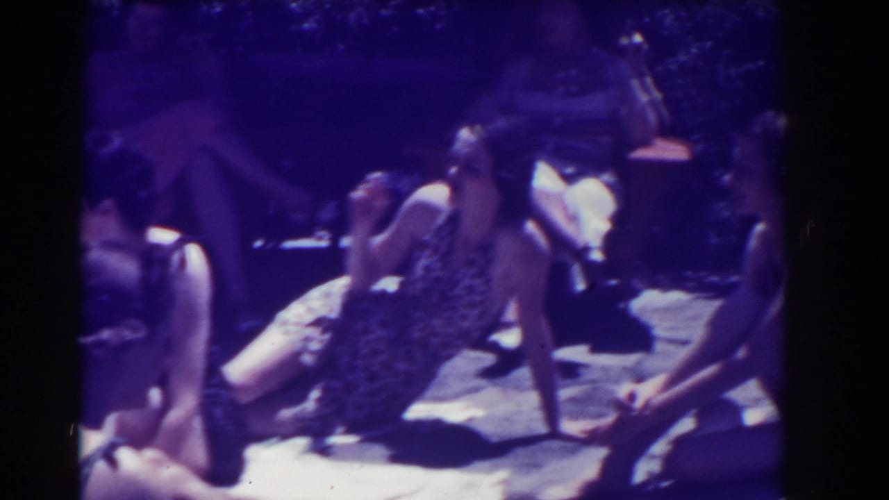 Several women sit outdoors in swimsuits, with one holding a cigarette near her face.
