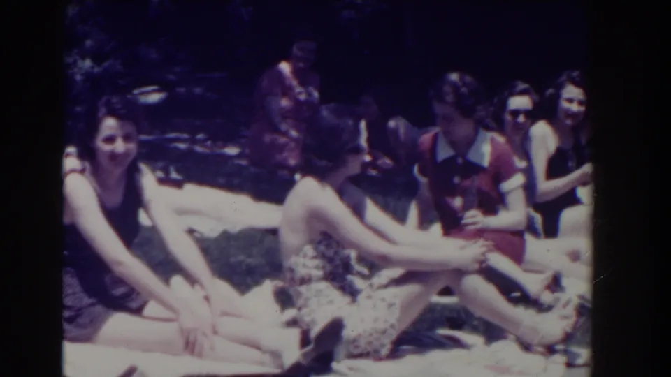 Group of women in swimwear sit together on towels in a sunny Southampton garden, some facing the camera.