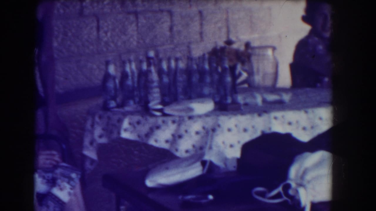 A table with many bottles sits in front of a textured wall, with a person partly visible.