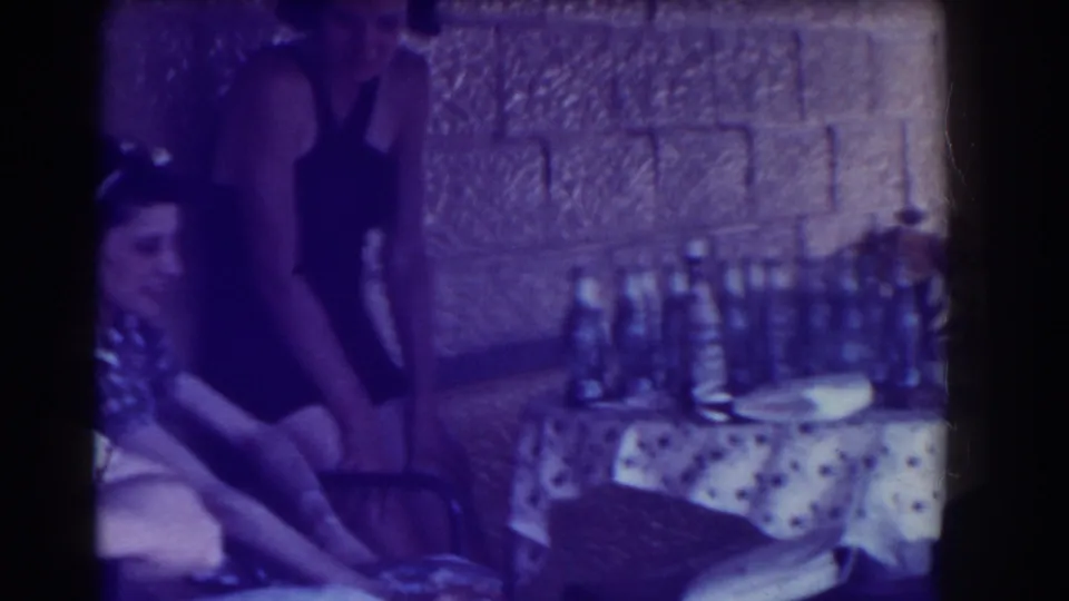 Young women in 1930s attire sit and stand around a bottle-filled table in a Southampton interior.