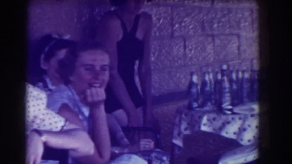 A smiling young woman faces the camera as others gather near the bottle-covered table in the 1937 Southampton clip.