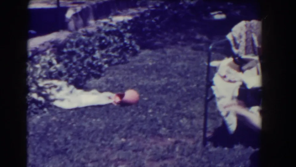 The frame shows a backyard lawn in Southampton with a seated adult, garden planting, a cloth on the grass, and a ball near the center.
