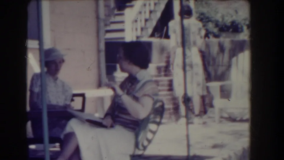 On a Southhampton porch in 1937, a woman in a striped top turns toward another seated woman as the conversation continues.