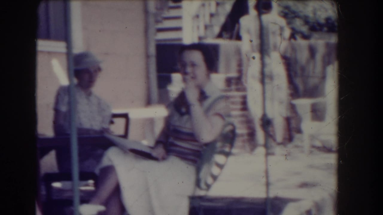 Two women seated on a patio, one reading and one holding a drink.