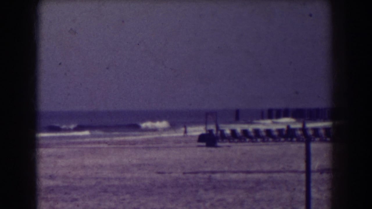 Empty beach with surf, vacant chairs, and a distant pier or jetty.