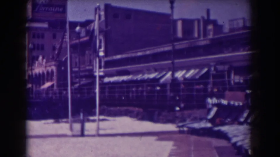 Atlantic City boardwalk storefront view from 1938, with awnings, upright poles, snow patches, benches, and the Lorraine sign at left.