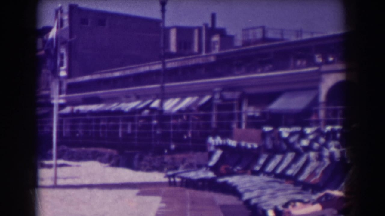 Rows of beach lounge chairs in front of arched boardwalk buildings and striped awnings.